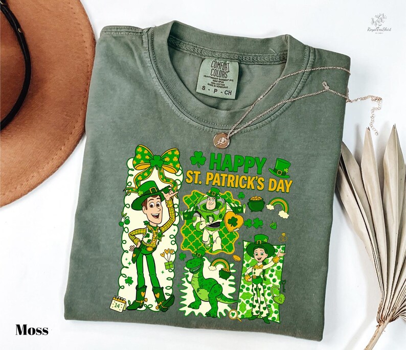 A green t-shirt with a cartoon character and text printed on it, along with a brown hat and some leaves.