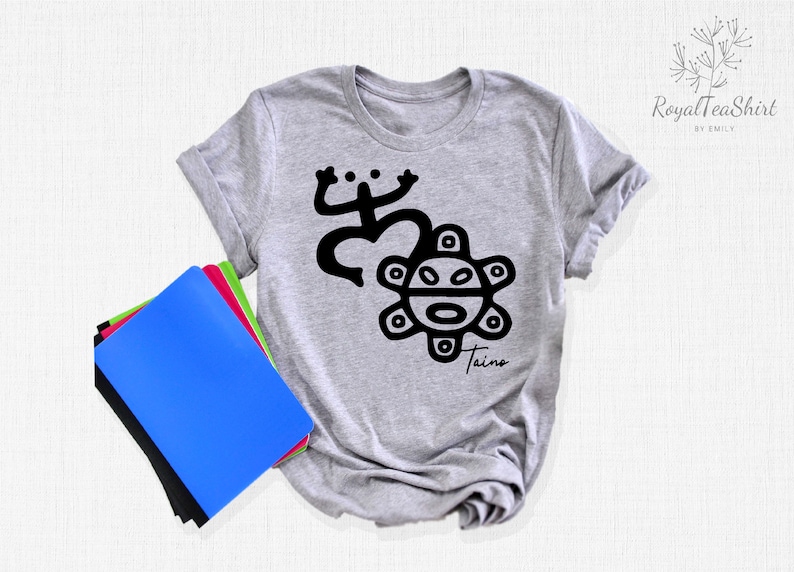May include: A gray t-shirt with a black graphic of a stylized sun with a face and a frog-like figure. The text "Taino" is printed below the graphic.