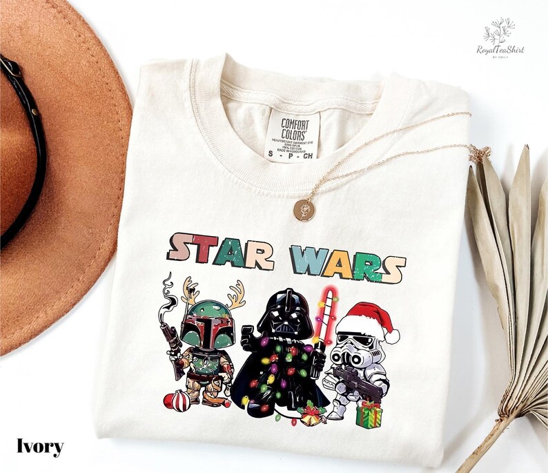 A white t-shirt with a colorful graphic design featuring characters from the Star Wars franchise, including Darth Vader, Stormtrooper, and an elf.