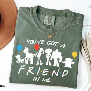 A green t-shirt with a printed design of characters from the TV show "Friends" and the text "You've got a friend in me" printed on it.