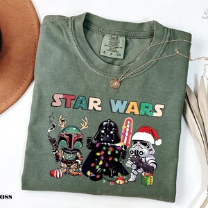 A green t-shirt with a Star Wars graphic design featuring three characters: a knight, a dragon, and a stormtrooper, along with Christmas decorations.