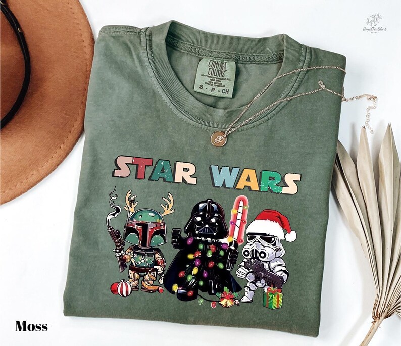 A green t-shirt with a Star Wars graphic design featuring three characters: a knight, a dragon, and a stormtrooper, along with Christmas decorations.