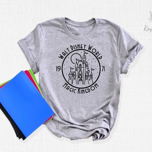 May include: A gray t-shirt with a black and white graphic of Cinderella's castle in a circle with the text "Walt Disney World 1971 Magic Kingdom".