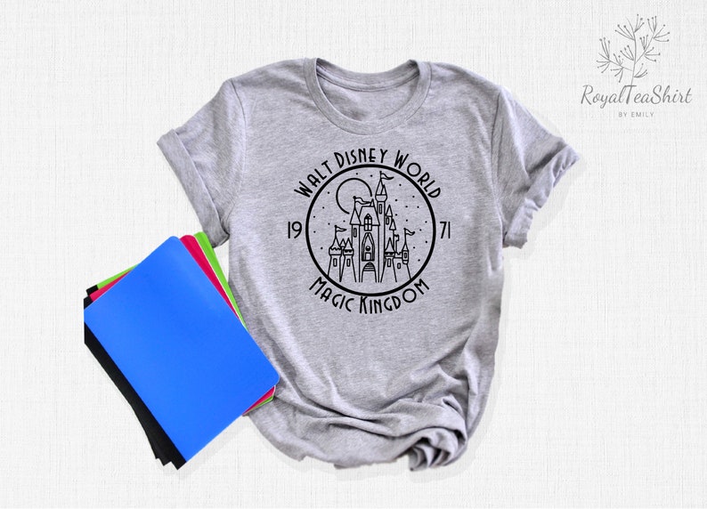 May include: A gray t-shirt with a black and white graphic of Cinderella's castle in a circle with the text "Walt Disney World 1971 Magic Kingdom".