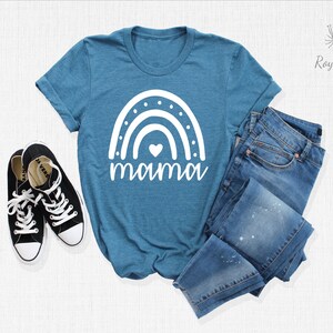 May include: A teal blue t-shirt with a white rainbow and the word "mama" printed on the front. The rainbow has a small white heart in the centre.