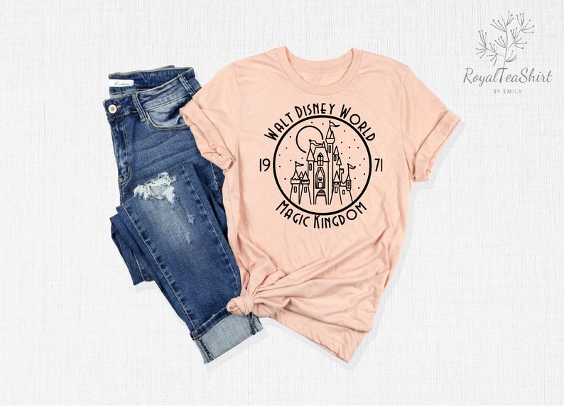 May include: A peach-colored t-shirt with a black graphic of Cinderella's castle in a circle with the text "Walt Disney World 1971 Magic Kingdom".