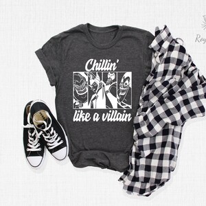 K&ouml;nnte beinhalten: Ein dunkelgraues T-Shirt mit einer wei&szlig;en Grafik von Disney-Schurken. Der Text auf dem Shirt lautet "Chillin' like a villain".