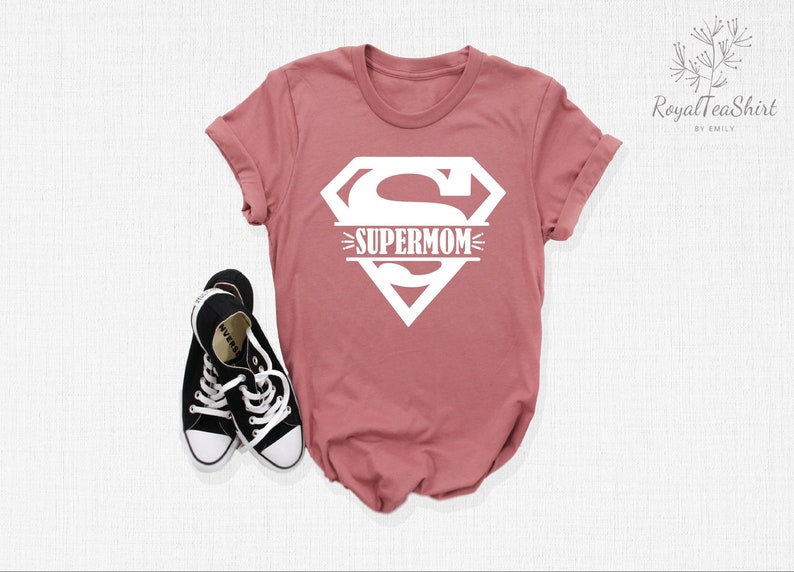 K&ouml;nnte beinhalten: Ein staubiges rosafarbenes T-Shirt mit einem wei&szlig;en Superman-Logo und dem Text "SUPERMOM" auf der Vorderseite.