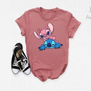 K&ouml;nnte beinhalten: Ein mauvefarbenes T-Shirt mit einem Aufdruck von zwei pinkfarbenen und blauen Comicfiguren. Die Figuren sind Stitch und Angel aus dem Disney-Film Lilo & Stitch.