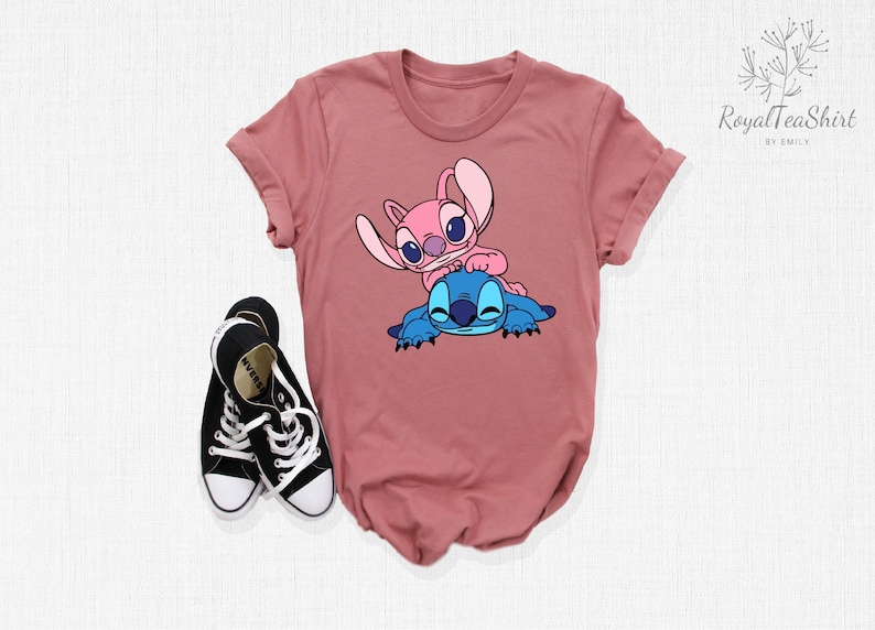 K&ouml;nnte beinhalten: Ein mauvefarbenes T-Shirt mit einem Aufdruck von zwei pinkfarbenen und blauen Comicfiguren. Die Figuren sind Stitch und Angel aus dem Disney-Film Lilo & Stitch.