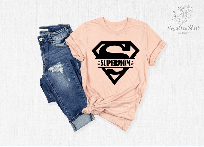 K&ouml;nnte beinhalten: Ein pfirsichfarbenes T-Shirt mit einem schwarzen Superman-Logo und dem Text "SUPERMOM" im Logo.