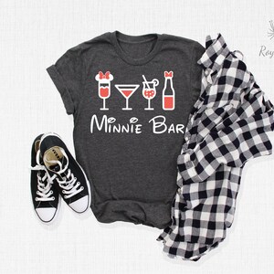 May include: A dark gray t-shirt with a white graphic of a Minnie Mouse head with a red bow and four red drink icons. The text "Minnie Bar" is written in white below the icons.