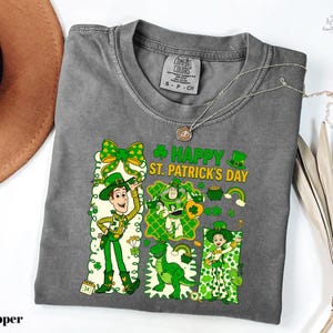 A gray t-shirt with a cartoon character design and text related to St. Patrick's Day, along with a necklace and a hat.