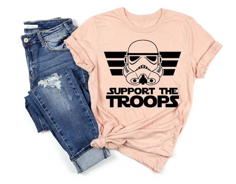 May include: A pink t-shirt with a black graphic of a Star Wars Stormtrooper helmet with the text "Support the Troops" underneath.