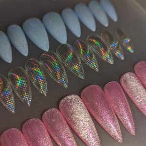 May include: A set of three different styles of fake nails. The first row features light blue nails with a shimmer finish. The second row features iridescent holographic nails. The third row features pink nails with a glitter finish.