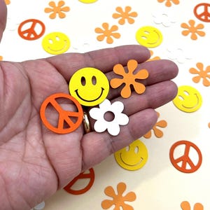May include: Assortment of colorful paper confetti featuring peace signs, smiley faces, and flower shapes in orange, yellow, and white.