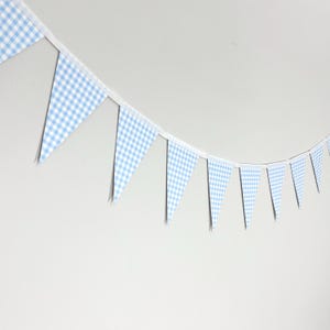 May include: A string of light blue and white checkered pennant flags. The triangular flags are attached to a white ribbon and hang against a white background. The flags are evenly spaced.