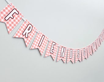 May include: A banner with pennant flags spelling out "FRIENDSGIVING" in a playful font. The flags have a pink and white gingham pattern with brown outlines. The banner is strung on a white string against a light gray background.