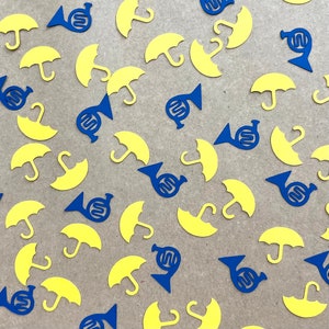 May include: A collection of blue and yellow paper cutouts scattered on a brown surface. The cutouts are in the shapes of umbrellas and French horns.