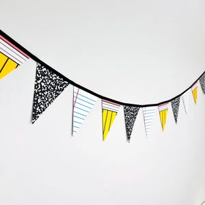 May include: A decorative bunting banner featuring triangular pennants with alternating patterns of black and white composition notebook speckles, yellow pencils with pink erasers, and white lined notebook paper with blue horizontal lines.