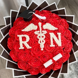 May include: A red rose bouquet arranged in a circular shape, featuring white accents spelling "RN" and a medical symbol. Includes a graduation cap and a rolled diploma. The bouquet is wrapped in decorative paper.