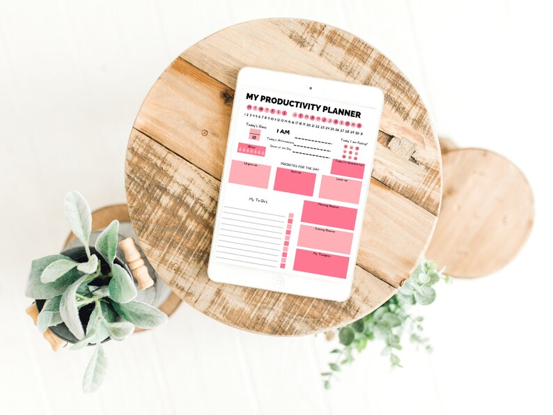 Op de afbeelding: Een digitale productiviteits planner op een tablet met een roze en wit ontwerp. De planner bevat secties voor dagelijkse doelen, takenlijsten en een stemmingstracker.