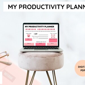 Op de afbeelding: Een laptopcomputer die een roze en witte productiviteits planner toont met de tekst "MY PRODUCTIVITY PLANNER" op het scherm. De laptop staat op een roze kruk met gouden poten. De tekst "DIGITAL PDF" staat in een roze cirkel op een witte achtergrond.