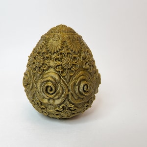 May include: A gold-colored egg-shaped ornament with intricate floral and rose designs.
