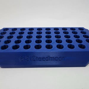 May include: A blue, rectangular ammunition holder with numerous circular openings. The text "6.5 Creedmoor" is embossed on the side. The holder is designed to organize and store ammunition.