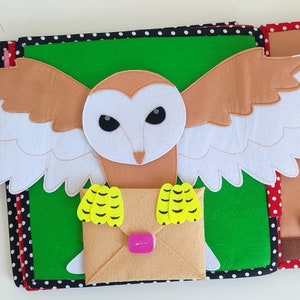 May include: A felt owl with brown and white wings holding a brown envelope with yellow accents. The owl is on a green background with black and white polka dots.
