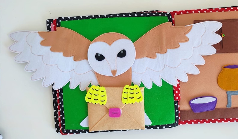 May include: A felt owl with brown and white wings holding a brown envelope with yellow accents. The owl is on a green background with black and white polka dots.