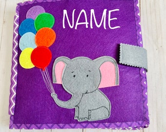 May include: Purple felt book with a gray elephant holding colorful balloons. The book has a flap on the side and the text "NAME" is embroidered on the front.