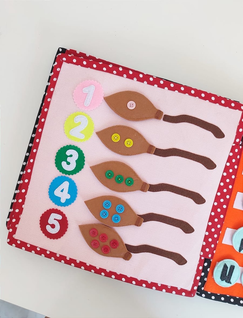 May include: A pink felt book with red polka dots on the cover. The book has five pages with numbers 1 through 5 and brown felt leaves with buttons on each page.