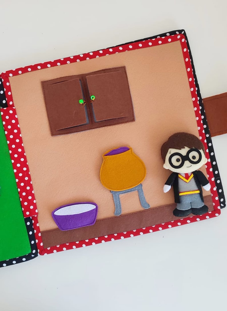 May include: A felt book page with a brown cabinet, a purple bowl, a yellow cauldron on a gray stand, and a character from the Harry Potter series wearing a black robe and glasses.