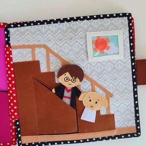 May include: A felt book page with a brown staircase, a character with glasses and a black robe, and a white dog with brown ears. The background is a white and gray pattern.