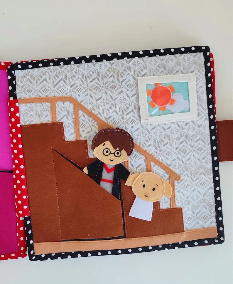 May include: A felt book page with a brown staircase, a character with glasses and a black robe, and a white dog with brown ears. The background is a white and gray pattern.