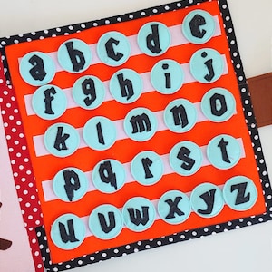 May include: A felt alphabet book with a bright orange background and white stripes. Each letter is on a light blue circle with black stitching. The letters are in a black font.