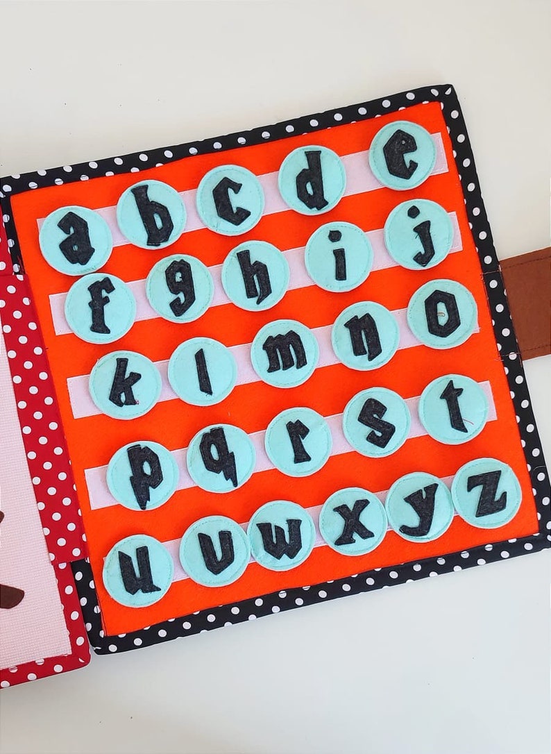 May include: A felt alphabet book with a bright orange background and white stripes. Each letter is on a light blue circle with black stitching. The letters are in a black font.