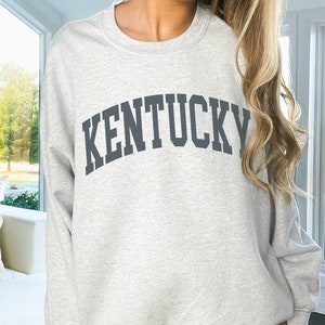 May include: A gray sweatshirt with the word "KENTUCKY" printed in a large, dark gray, arched font.