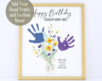 May include: A framed print with a gold border features a bouquet of watercolor flowers and two handprints in blue and purple. The text reads "Happy Birthday" and includes space for a custom name. The bottom text says "Made with Love by: [Custom Name(s) Here]"