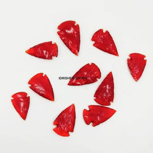 May include: Ten red arrowhead shaped stones, some with a slightly translucent appearance, arranged in a circle on a white background.