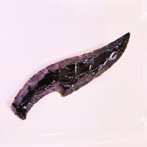 May include: A white ceramic mug with a black handle and the text "But First, Coffee" in a bold, black font. The mug is set against a blurred background, suggesting a cozy setting.