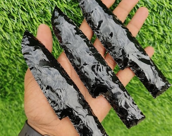 May include: Three black obsidian blades with sharp, serrated edges and a glossy, reflective surface. Each blade features a distinct, hand-knapped texture with irregular, layered patterns across the dark, glass-like material of the stone.