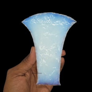 May include: A translucent, vase-shaped object with a flared top and a textured surface. The object is primarily white with hints of blue along the edges, held against a black background.