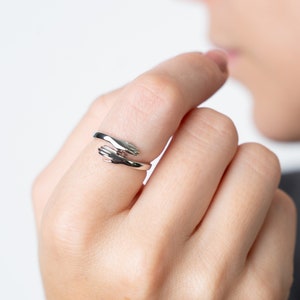 May include: A silver ring featuring two intertwined hands, a symbol of unity and connection.