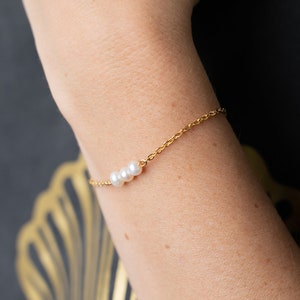 May include: A delicate gold chain bracelet with three small white pearls.