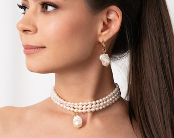 May include: A woman wearing a three-strand pearl choker necklace with a large pearl pendant. She is also wearing a pair of pearl drop earrings.