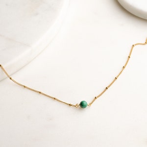 May include: A delicate gold chain necklace with a single green gemstone bead.