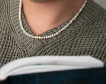 May include: A person wearing a green sweater with a pearl necklace. The person is reading a book.