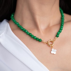 May include: A green jade bead necklace with a gold clasp and a white shell flower pendant.